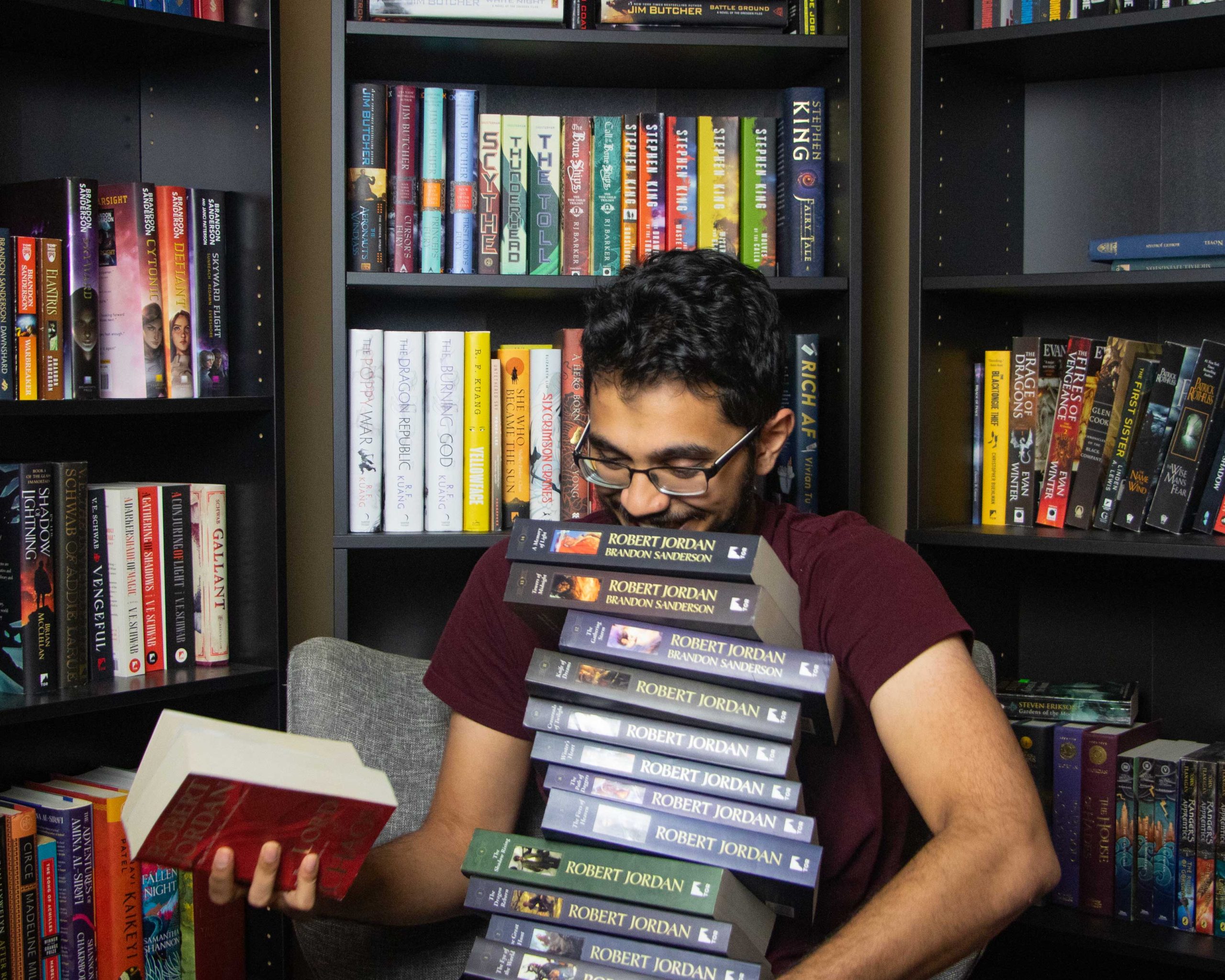 Aryan holding a stack of the Wheel of Time books in front of a full bookcase